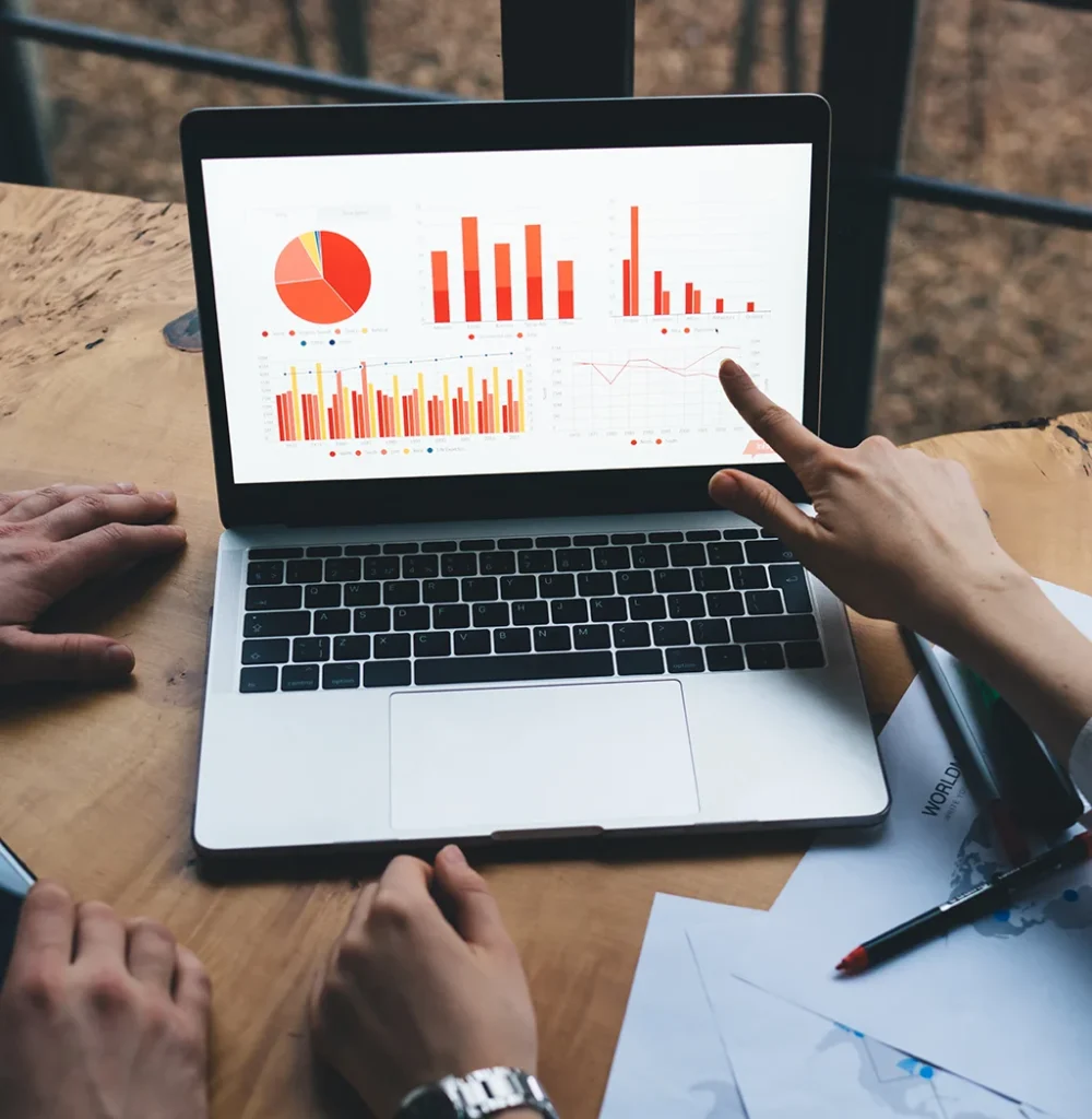 A hand pointing out charts and statistics being shown on a laptop